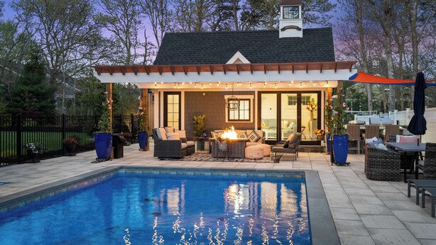 Un espace aménagé au bord de la piscine, comprenant un coin salon couvert, un foyer extérieur et du mobilier de jardin.