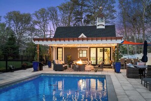 Un espace aménagé au bord de la piscine, comprenant un coin salon couvert, un foyer extérieur et du mobilier de jardin.