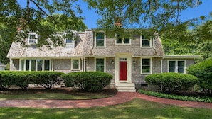 A two-story house with a red front door, a brick pathway leading to the entrance, and well-maintained greenery. - Game Room, Walk to Two Landings! (Wellfleet)