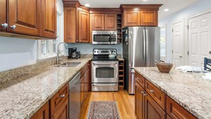 Una cocina con armarios de madera, electrodomésticos de acero inoxidable, encimeras de granito y un tapete estampado.
