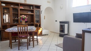 A living room with a dining table, chairs, a TV, a fireplace, and a bookshelf. - Al Primo Piano - Ischia (Forio)