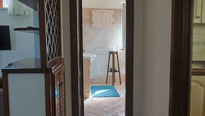 A hallway leading to a kitchen with a tiled backsplash, a wooden stool, and a blue mat on the floor. - Al Primo Piano - Ischia (Forio)
