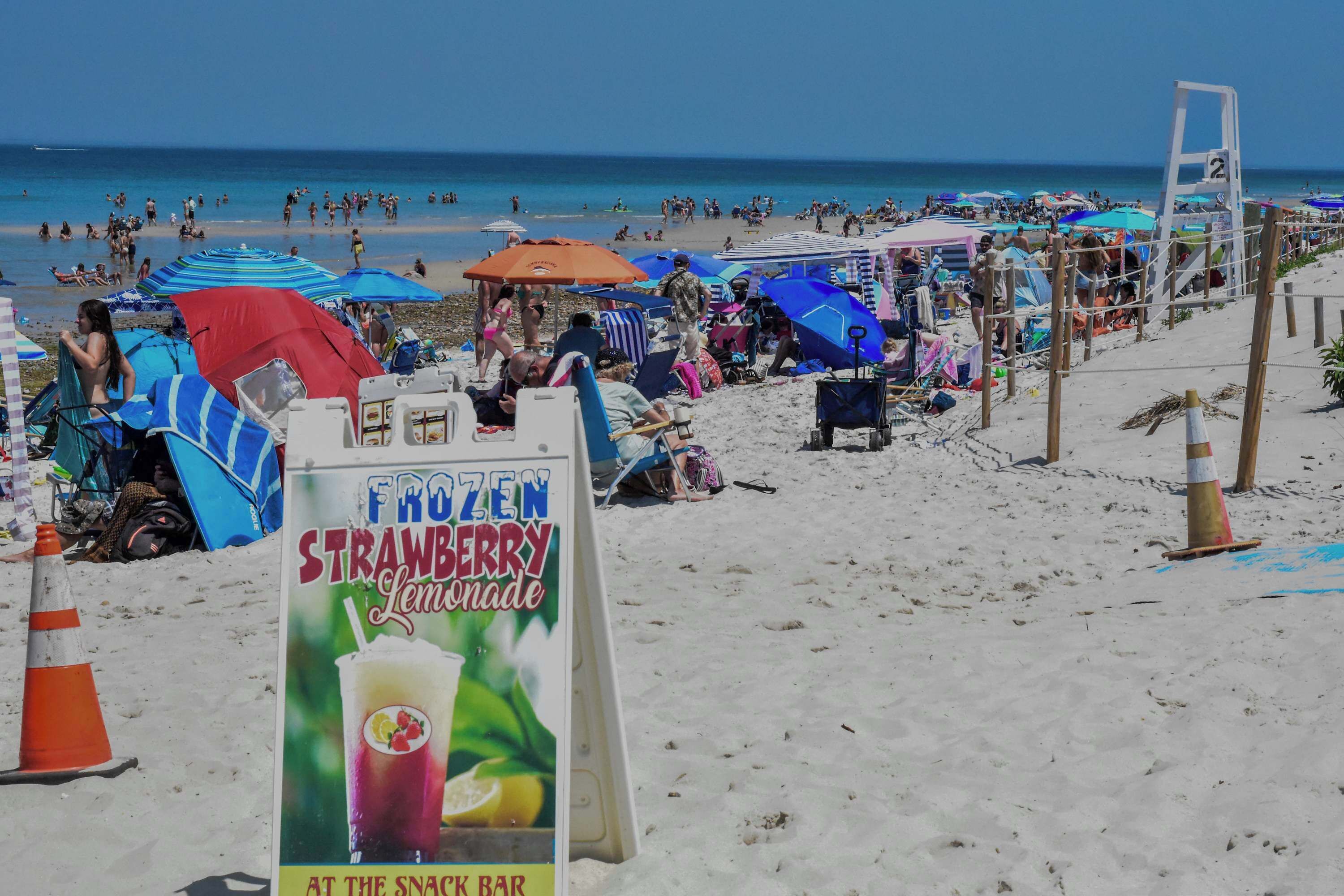 A beach scene with a sign for a frozen strawberry lemonade drink.