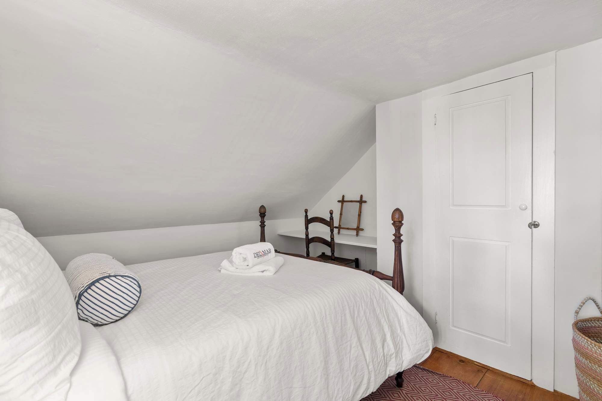 Une chambre avec un lit blanc, une tête de lit en bois, une porte blanche et une petite étagère avec une échelle.