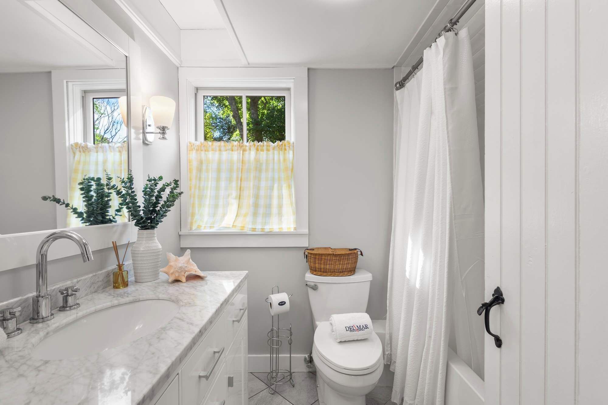 Een badkamer met een witte wastafel, een toilet en een raam met een geruit gordijn.