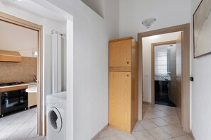 Uma cozinha com fogão, forno e máquina de lavar roupa, um armário de madeira e piso de azulejos.
