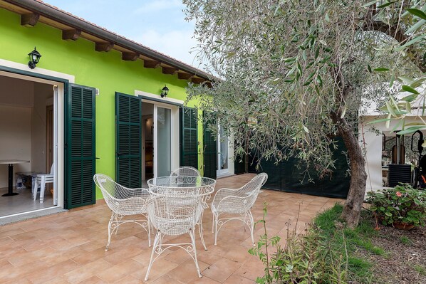 A patio with a table and chairs, a green wall, and a tree.