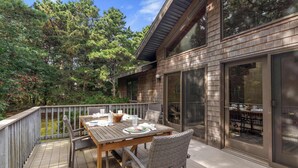 A wooden deck with a table set for dining, surrounded by wicker chairs. - Game Room, Central AC, Short Drive to Beaches! (Eastham)