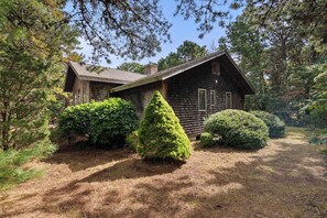 A rustic cabin surrounded by dense trees and well-maintained bushes. - Game Room, Central AC, Short Drive to Beaches! (Eastham)