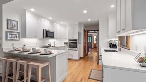 A modern kitchen with white cabinetry, stainless steel appliances, and a central island with stools. - Game Room, Central AC, Short Drive to Beaches! (Eastham)