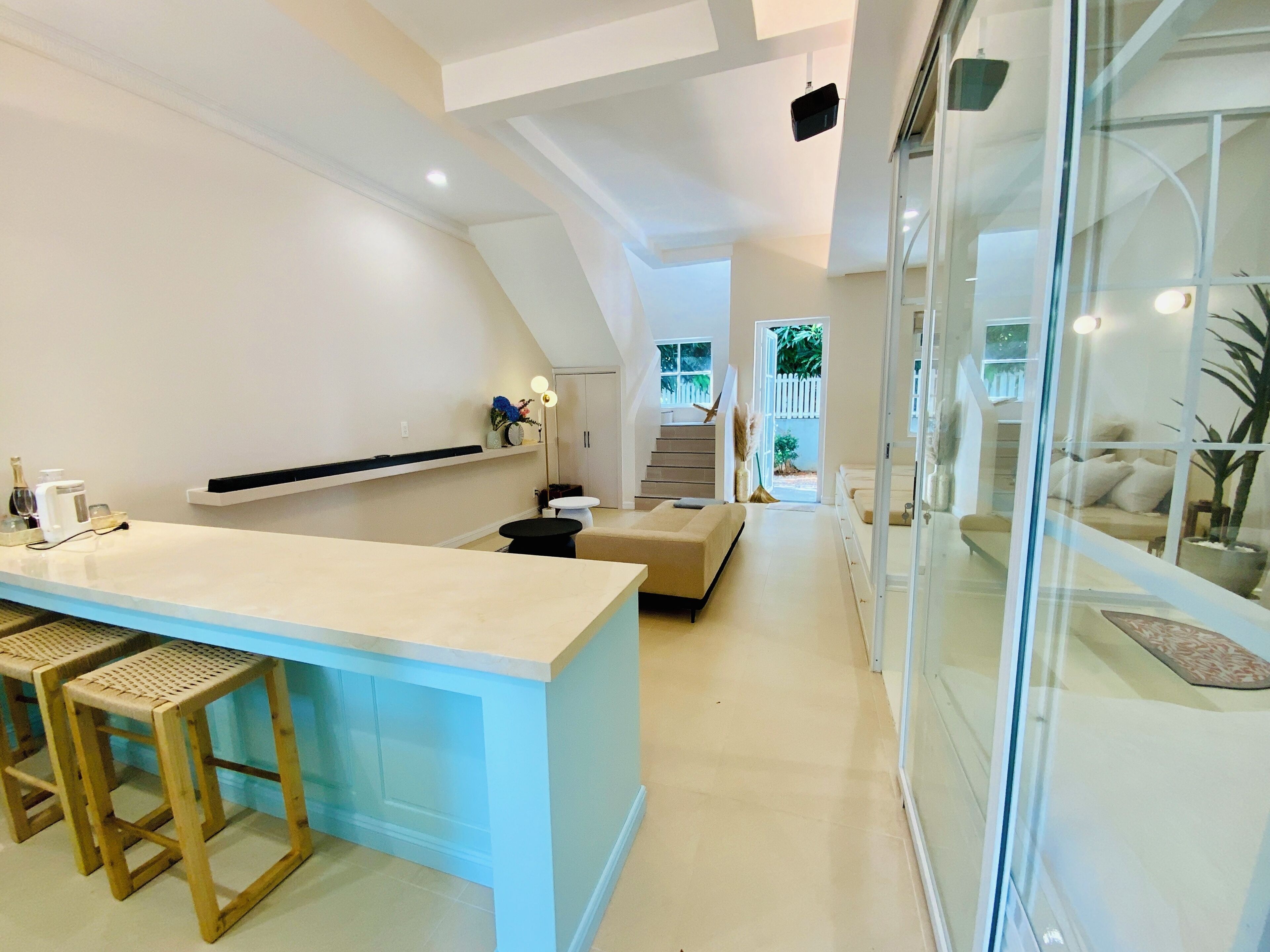 Una cocina moderna con una isla central, taburetes de bar y una escalera que lleva a un balcón.