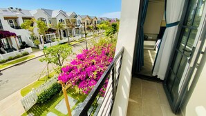 A balcony with a view of a row of townhouses, a white picket fence, and bougainvillea flowers. - Happy Stay Resort Novaworld Phan Thiet (Tien Thanh)