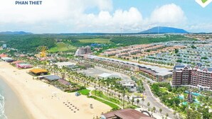 A coastal resort with a beachfront, a Ferris wheel, and a mix of hotel buildings. - Happy Stay Resort Novaworld Phan Thiet (Tien Thanh)