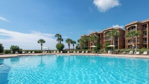 A clear blue pool with lounge chairs and palm trees, surrounded by a multi-story hotel building.