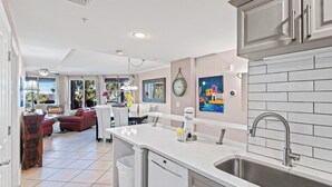 A modern kitchen with a dishwasher, sink, and a dining area with a red sofa and a table.