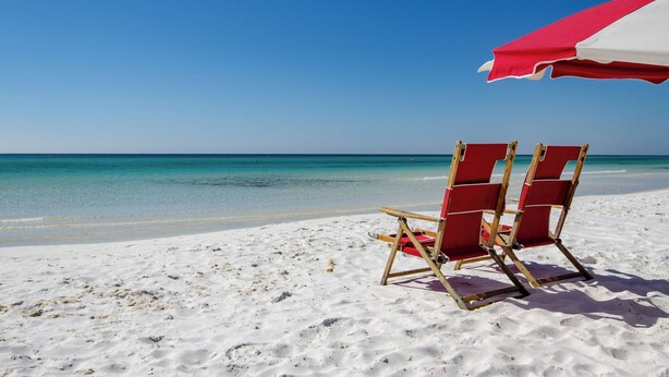 A beach with two red beach chairs and a red and white beach umbrella.