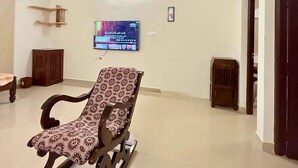 A spacious room with a wooden rocking chair, a television mounted on the wall, and a door leading to another room. - JUNGLE FARMS BY MAARK INN (Kanakapura)
