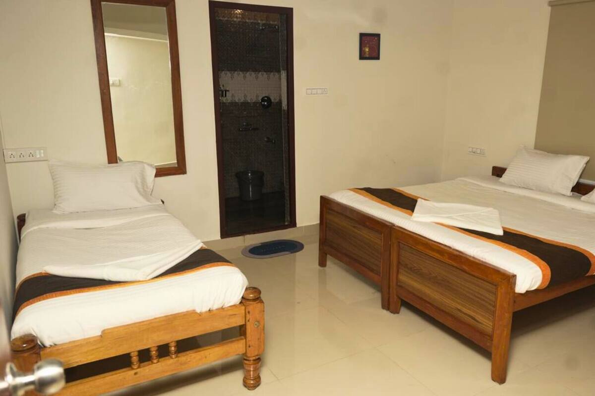 A hotel room with two wooden beds, white bedding, a mirror, a door, and a small wall-mounted picture.