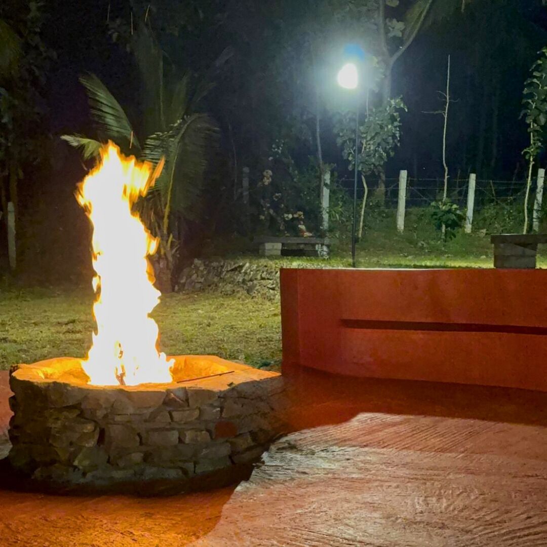A stone fire pit with flames, surrounded by a wooden bench and a stone wall.