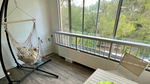 A balcony with a view of trees, a hanging chair, and a table with a green object. - Bright studio a few steps from the beach (Saint-Mandrier-sur-Mer)