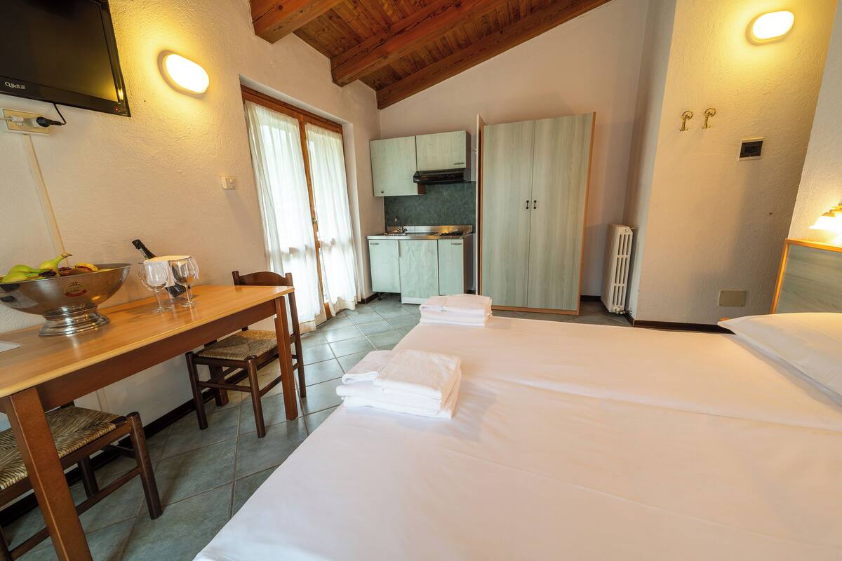 A room with a bed, a table with chairs, a kitchen area, and a television mounted on the wall.