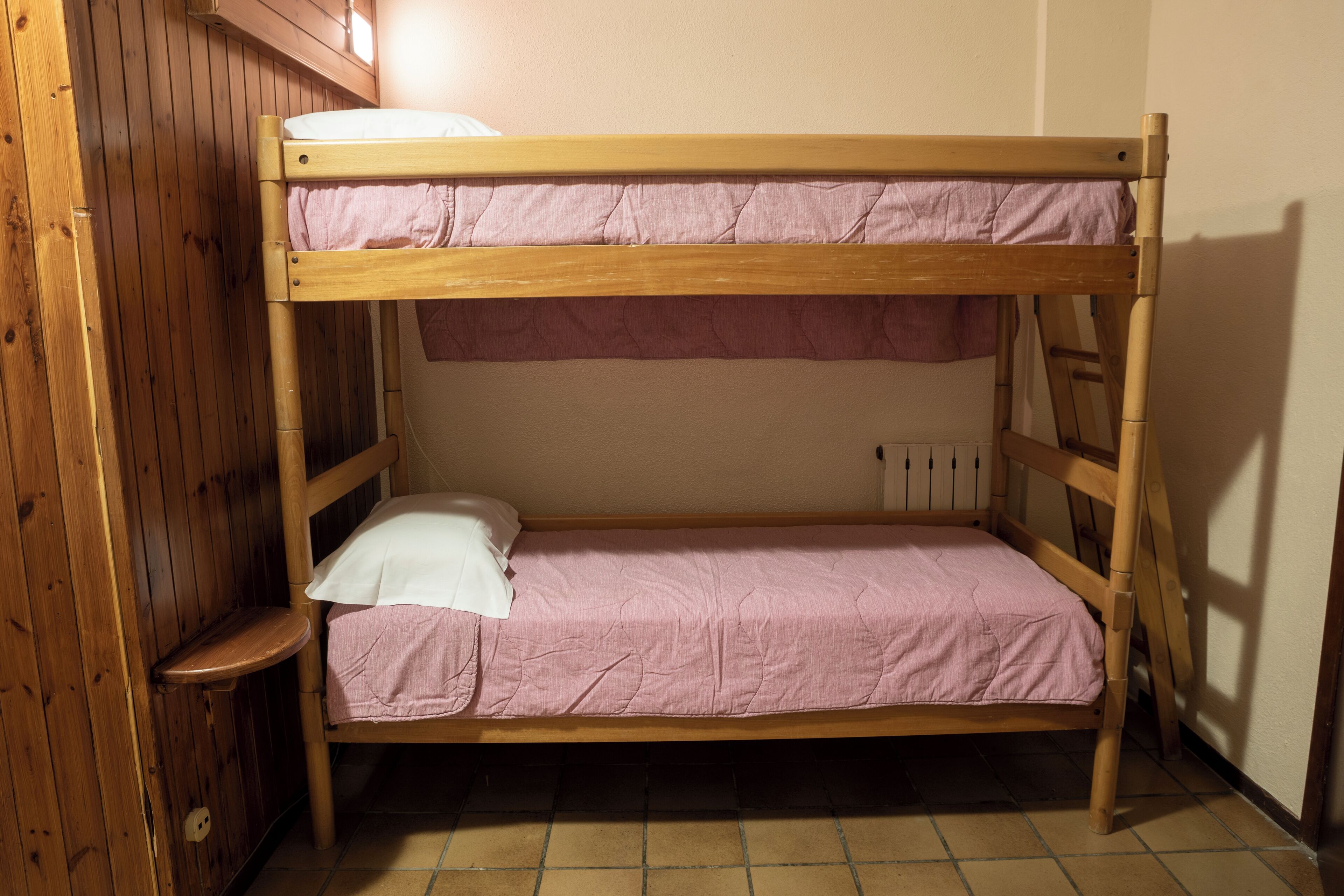 Un lit superposé avec un matelas rose et un oreiller blanc, dans une pièce aux murs en bois et au sol carrelé.