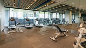 A modern gym with treadmills, weight machines, and a large window offering a city view. - Fully Furnished One Bedroom apartment in the heart of North York (North York)