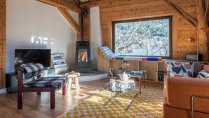 A cozy living room with a wooden ceiling, a fireplace, a television, and a large window offering a view of trees. - Spacious flat in the centre of Chamonix (Chamonix-Mont-Blanc)