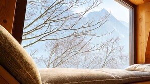 A wooden bench with a cushion, a window, and a view of bare trees and mountains. - Spacious flat in the centre of Chamonix (Chamonix-Mont-Blanc)