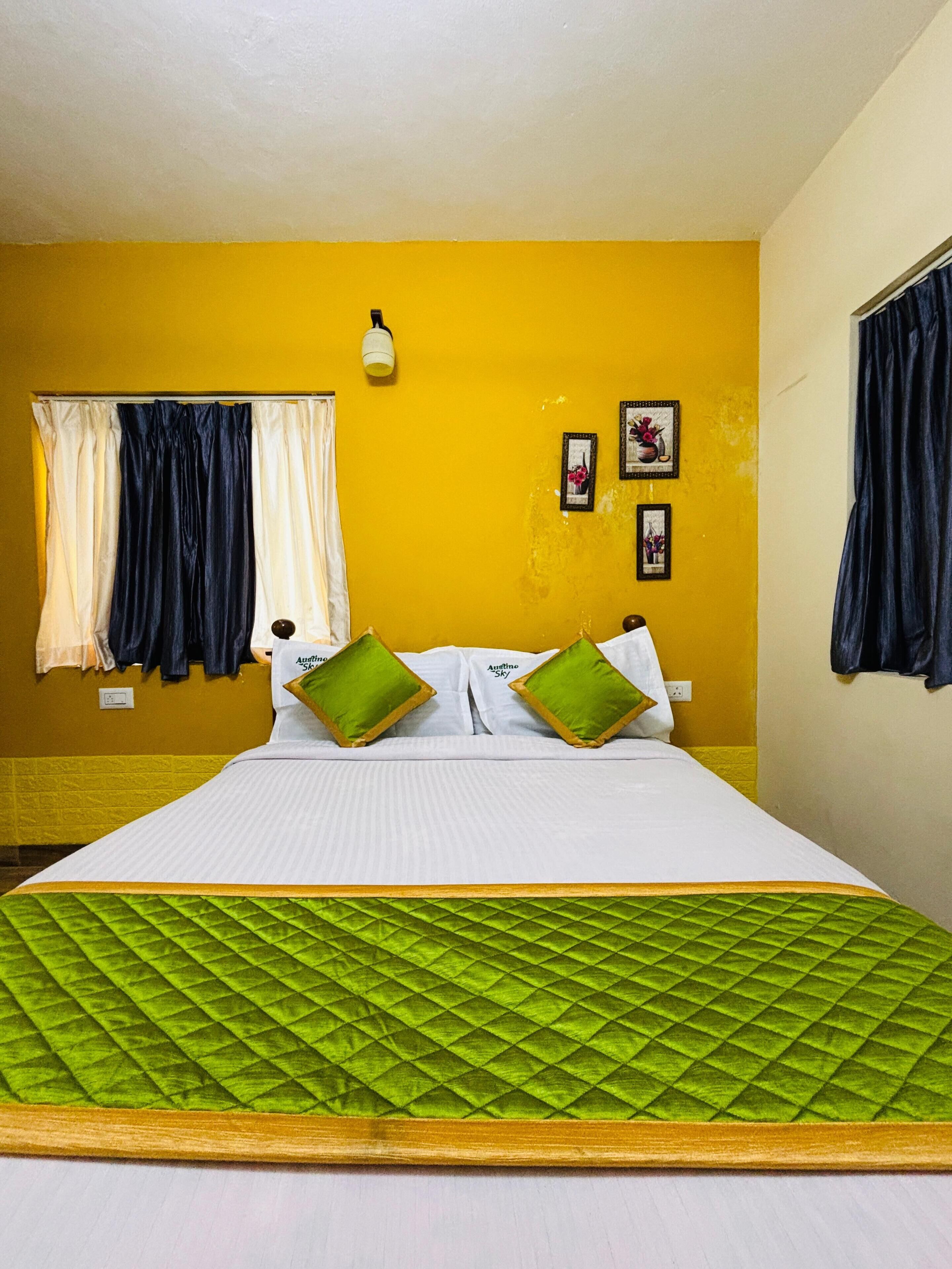 A hotel room with a bed, curtains, a wall-mounted light, and framed pictures.