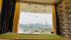Une chambre avec un grand lit, une vue sur le paysage urbain par la fenêtre et un mur en briques.