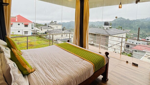 Une chambre avec un grand lit, une vue sur la ville et un balcon doté d’une balustrade.