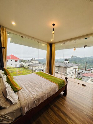 Een slaapkamer met een groot bed, uitzicht op een stadslandschap en een balkon met een leuning.