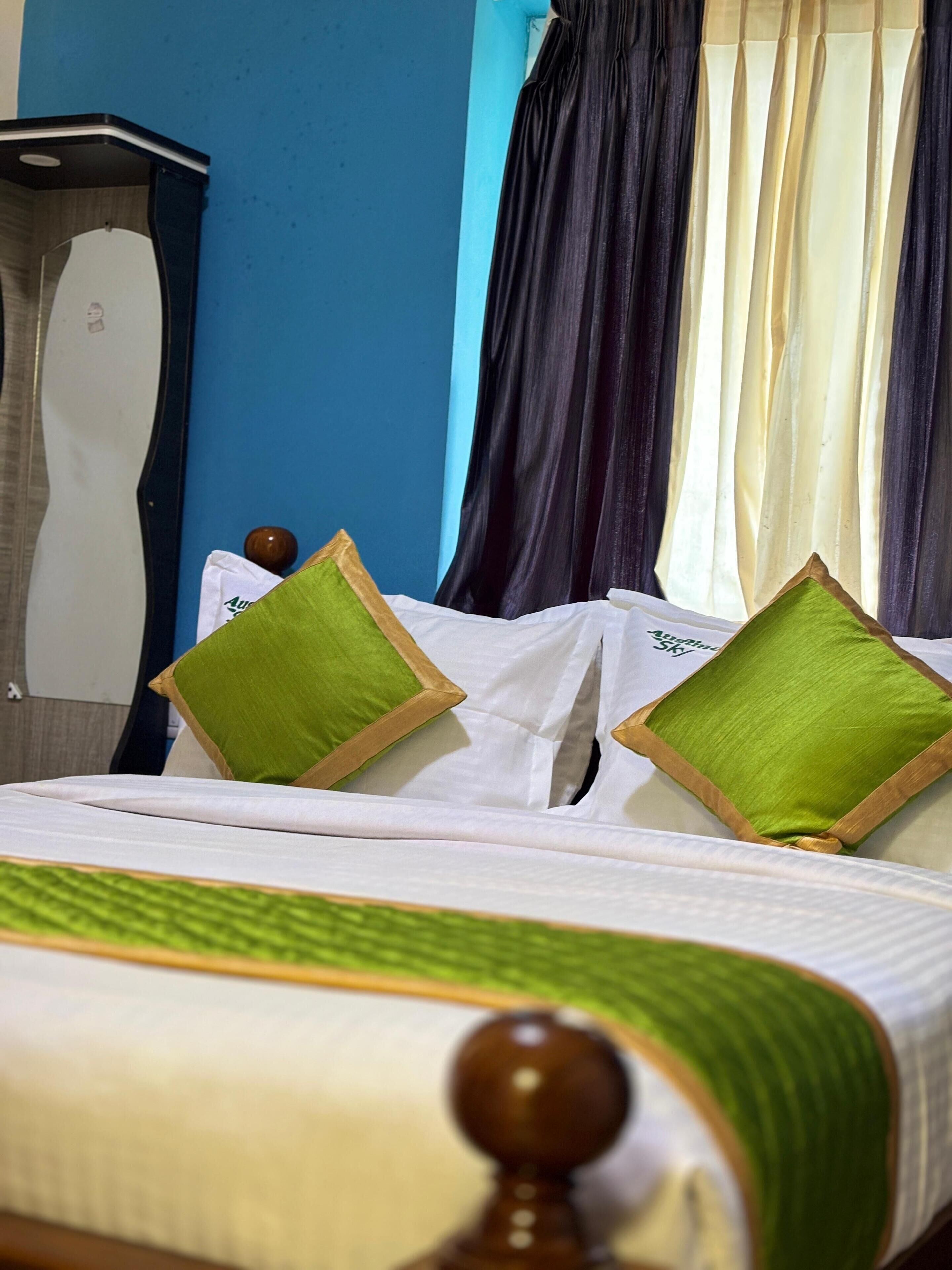 Een opgemaakt bed met groen-wit beddengoed, een houten hoofdbord en een blauwe muur met gordijn.