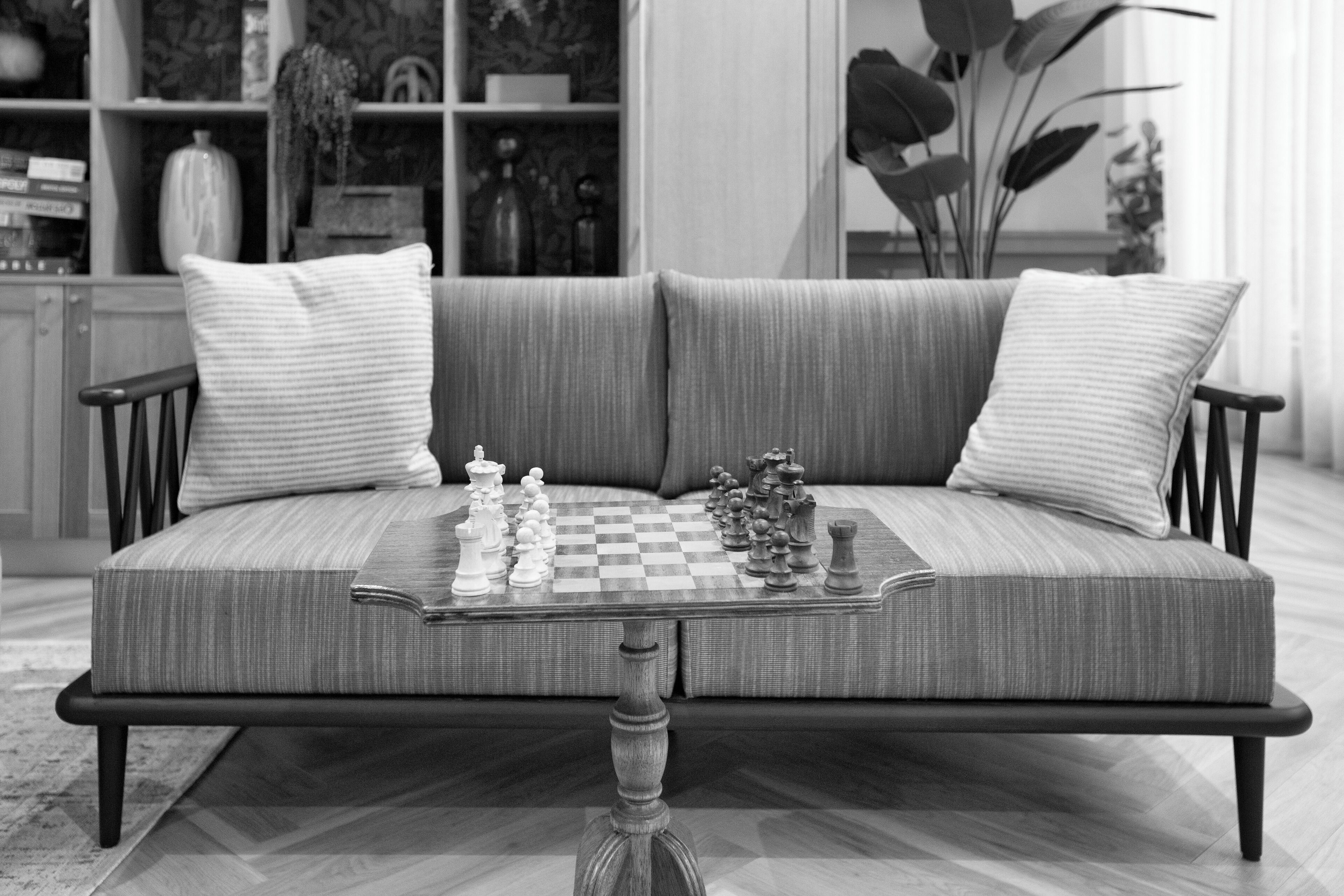 Un salon moderne avec un canapé, une table d’échecs et une bibliothèque en arrière-plan.