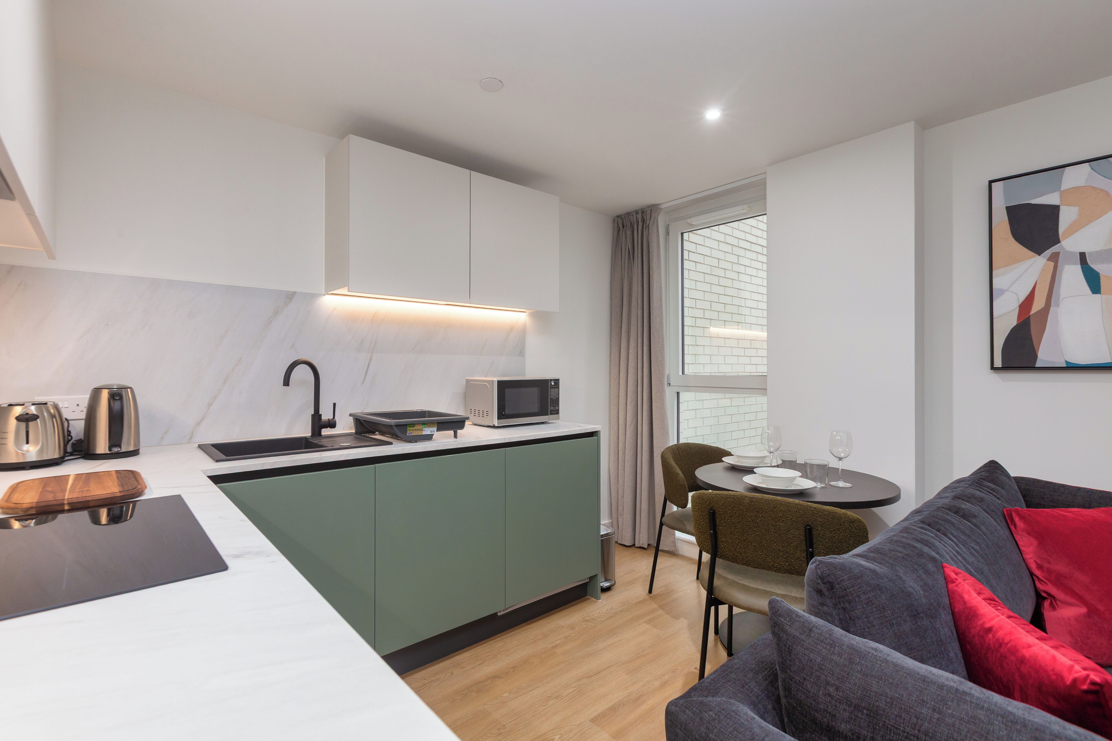 A compact living space with a kitchenette, dining area, and a sofa with red cushions.