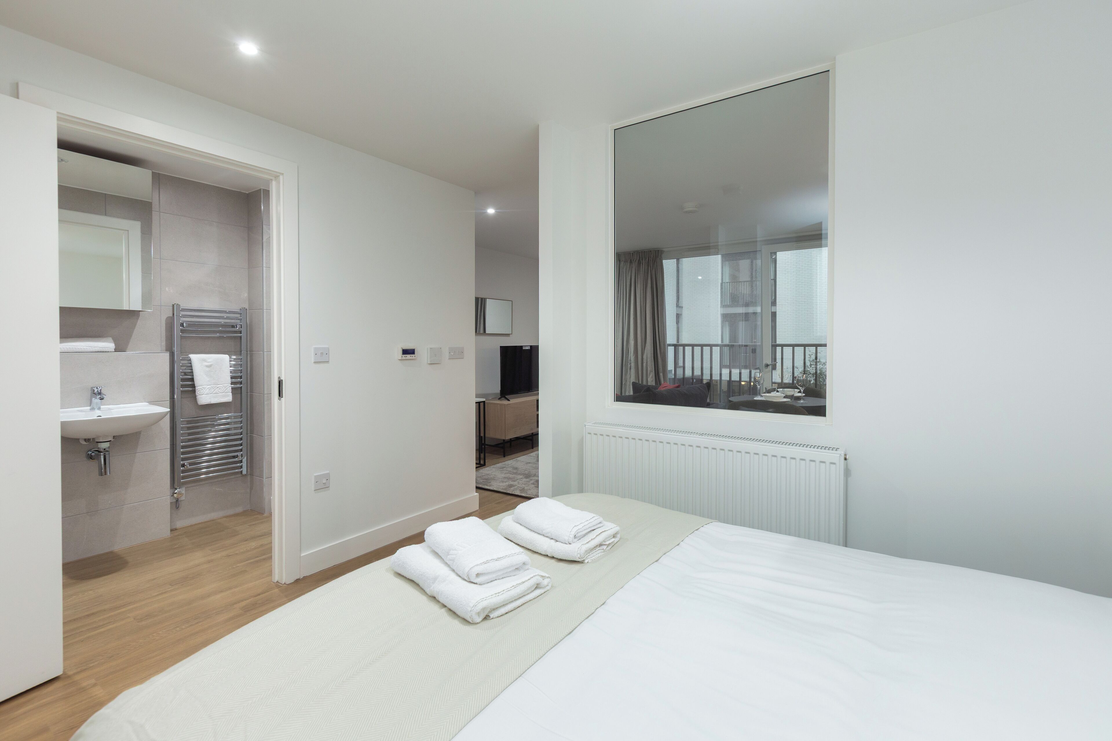 A modern hotel room with a large bed, a bathroom with a sink and towel rack, and a view of the outside balcony.