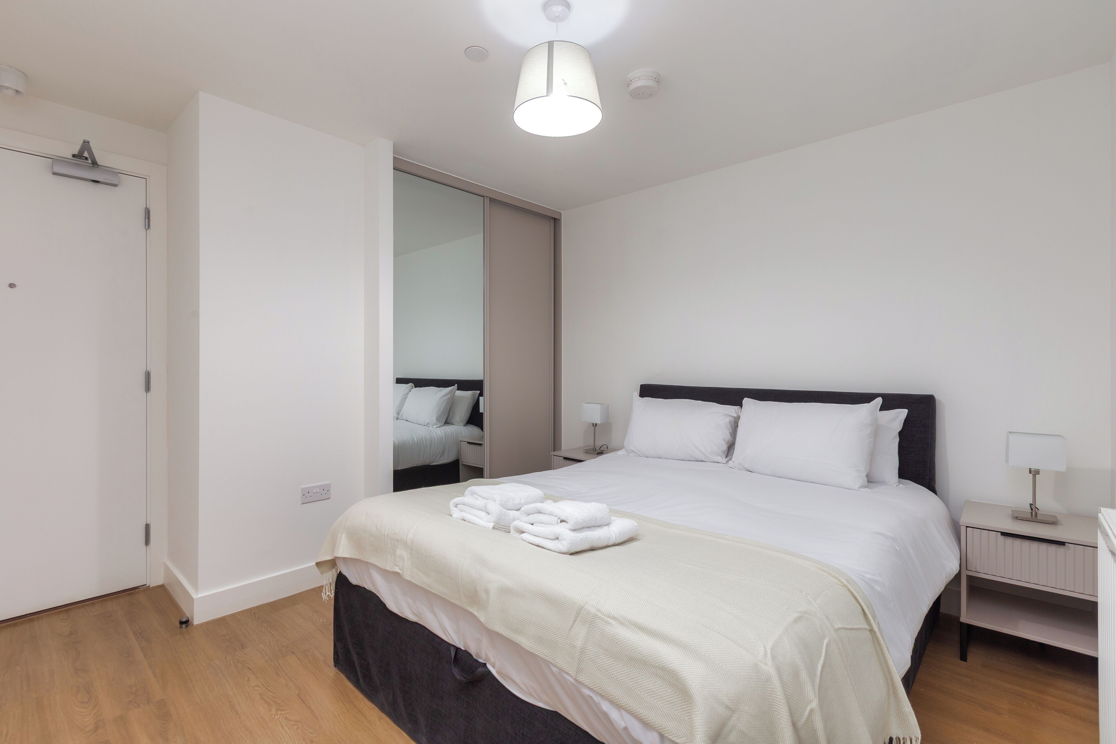 A neatly arranged hotel room with a large bed, bedside tables, a wardrobe, and a mirror.