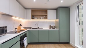 A modern kitchen with a built-in microwave, oven, and sink, light green cabinets, and a wooden countertop. - Mauve & Moss - Two Bedroom Apartment, Sleeps 4 (Bristol)