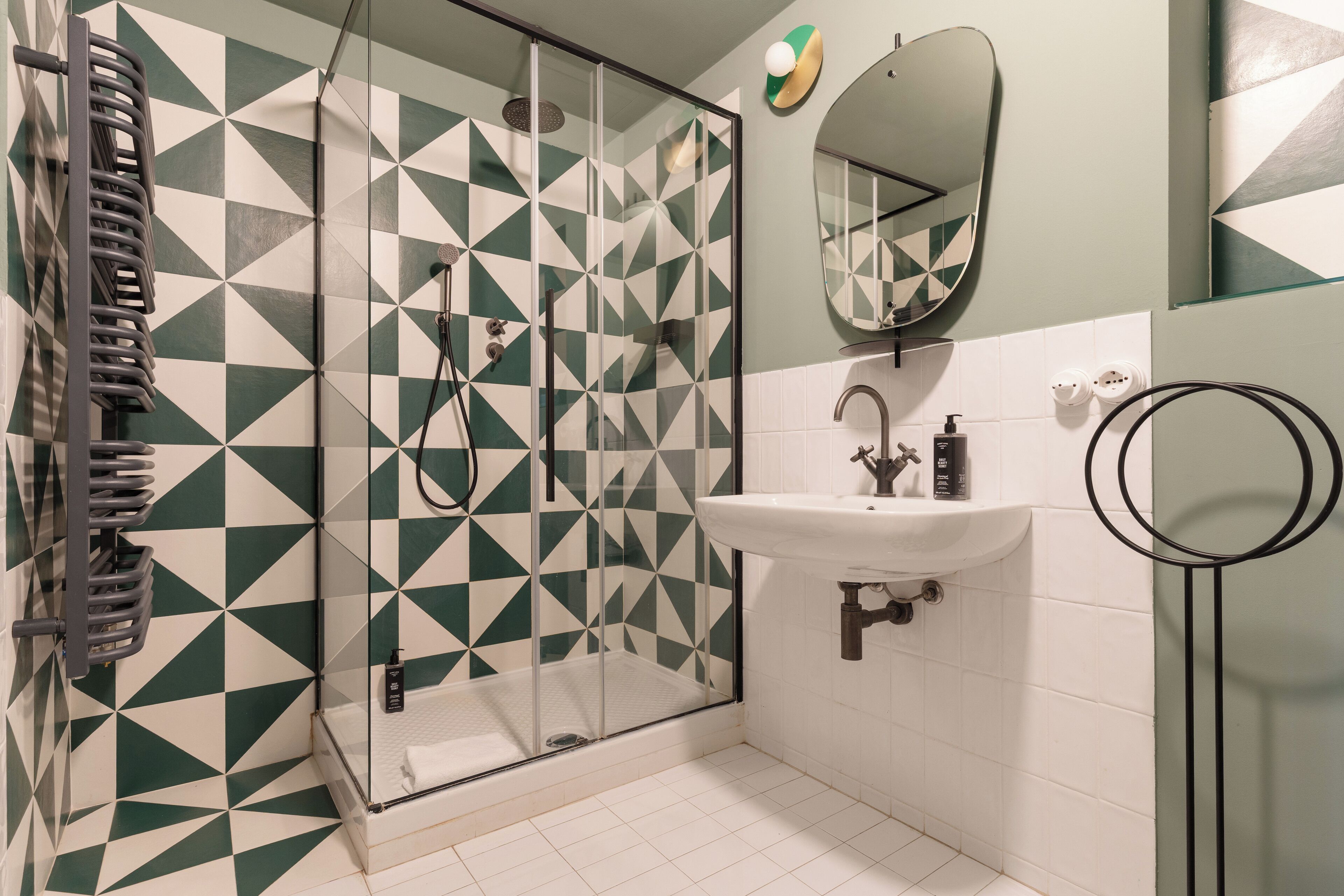 A bathroom with a geometric patterned wall, a glass shower enclosure, a white sink, and a mirror.