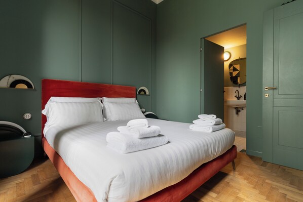 A neatly made bed with white linens and folded towels, a red headboard, and a wooden floor. - Brera Apartments in Gae Aulenti (Milan)