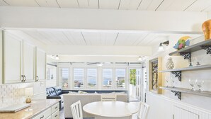 A kitchen with white cabinetry, a dining table with chairs, and a view of the outdoors through large windows. - Generator plus Beach, Pool, Golf, Tennis, Pickleball @ The Reef East End STX (Christiansted)