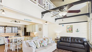 A spacious living area with a sofa, a dining table with chairs, a kitchen in the background, and a staircase leading to an upper level. - Generator plus Beach, Pool, Golf, Tennis, Pickleball @ The Reef East End STX (Christiansted)
