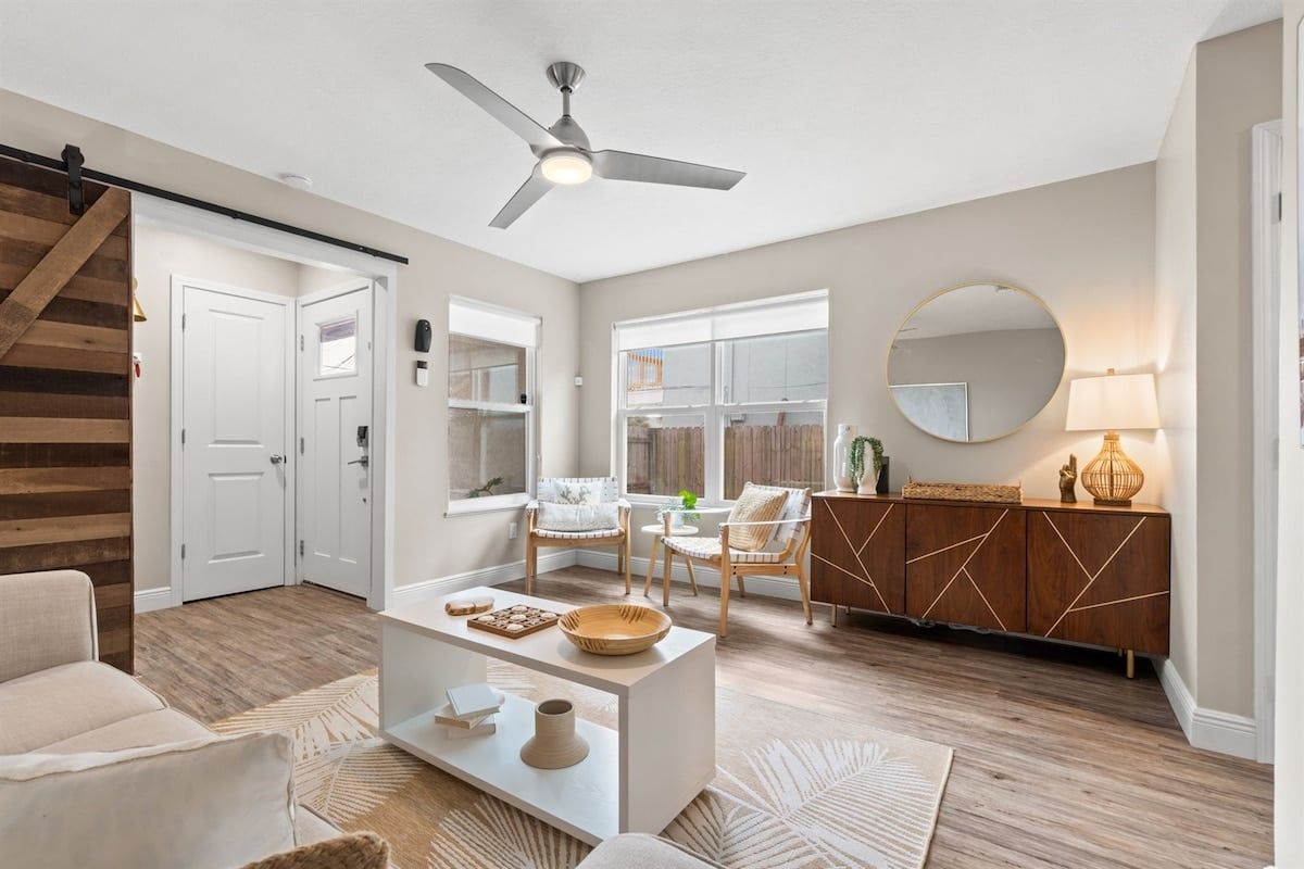 A modern living room with a ceiling fan, a sofa, a coffee table, and a dining area with chairs and a cabinet.