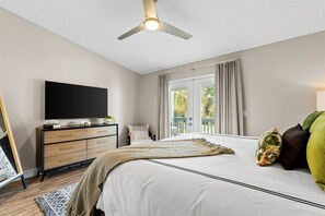Un dormitorio con cama, televisión, escritorio y ventilador de techo.