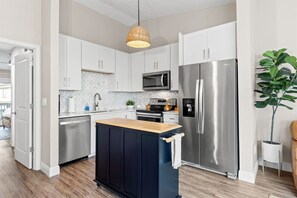 Una cocina moderna con armarios blancos, electrodomésticos de acero inoxidable, una isla de madera y una lámpara colgante.