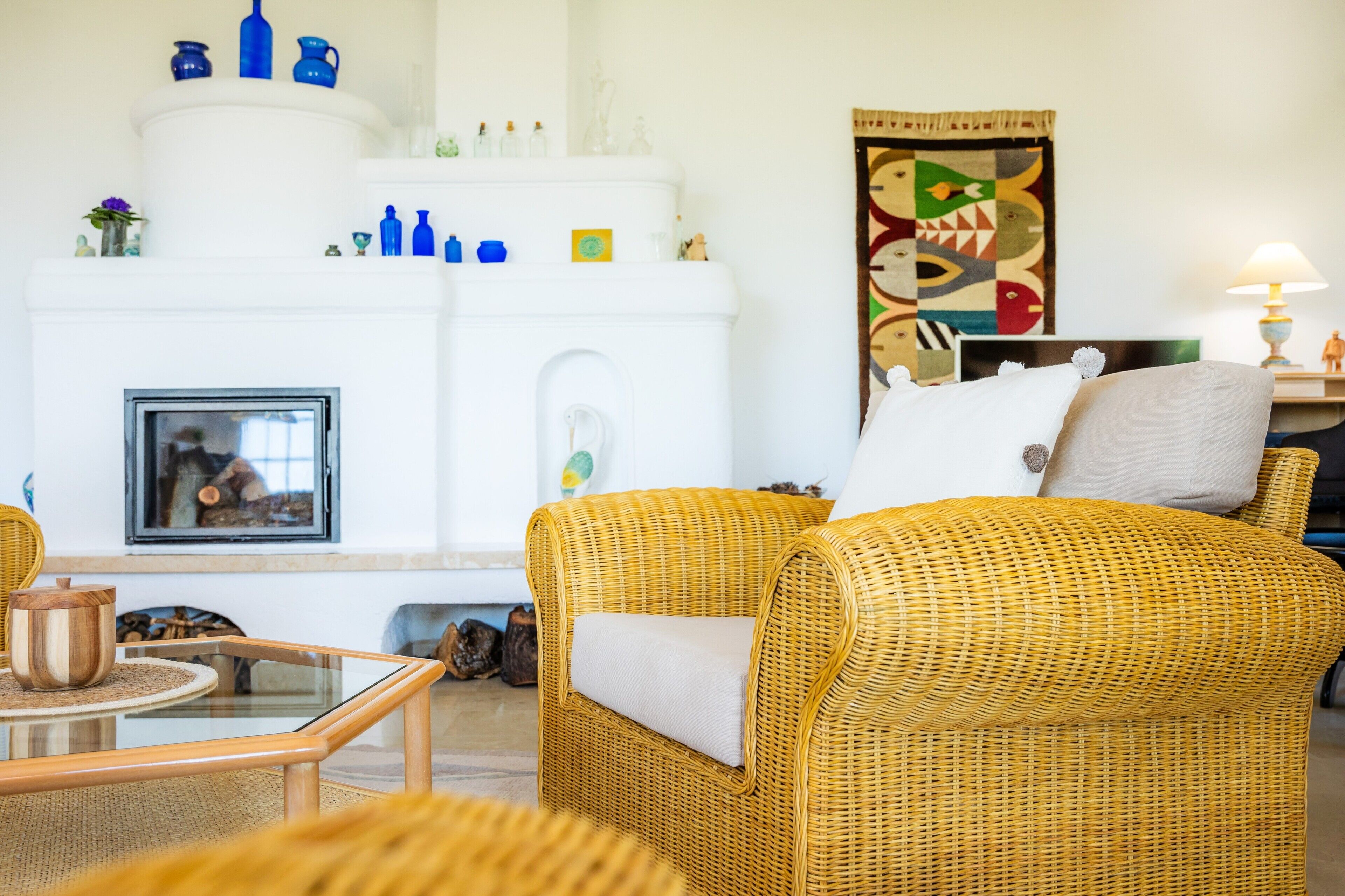 A living room with a fireplace, wicker furniture, and decorative items on shelves.