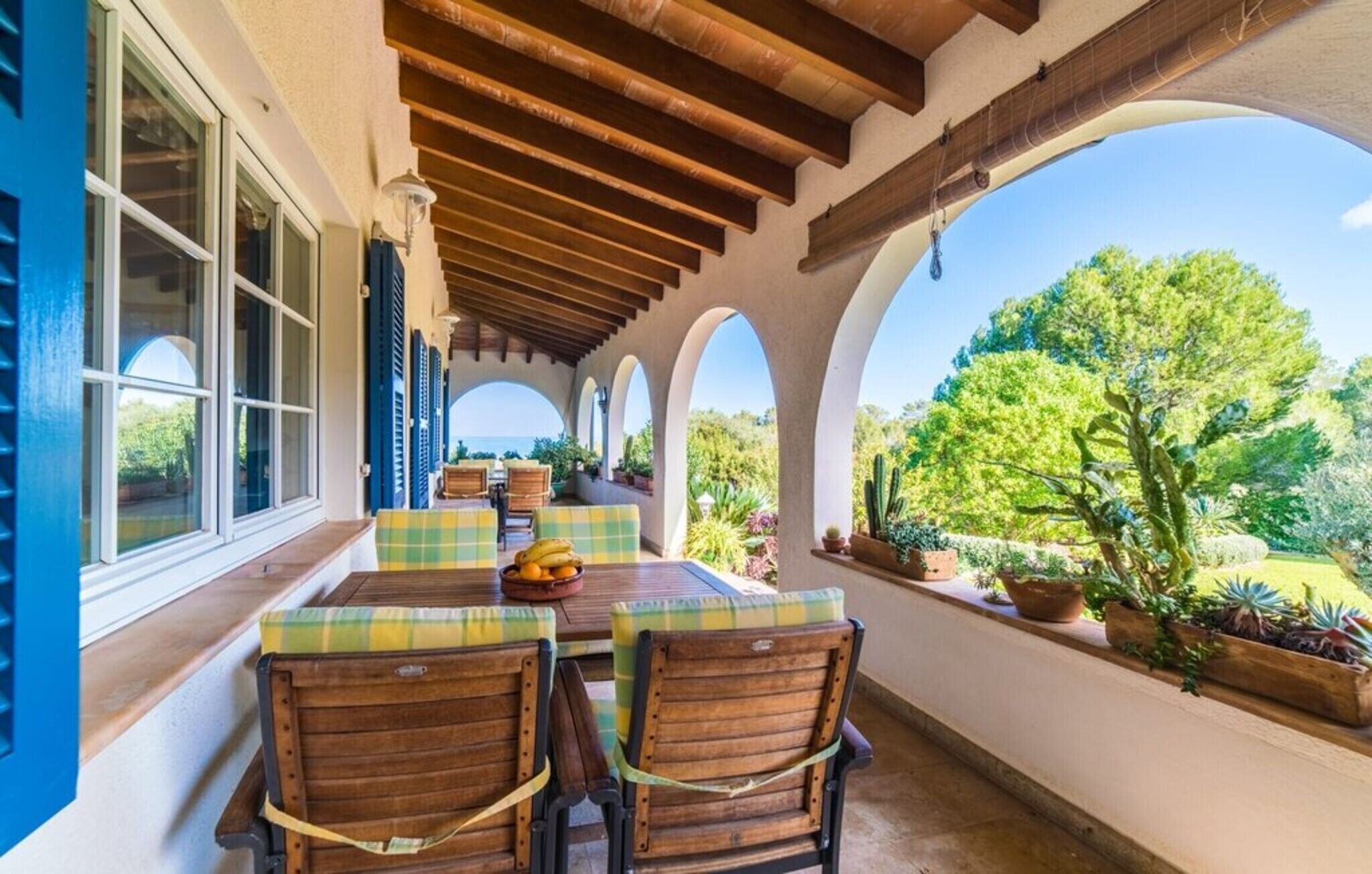 Une terrasse couverte avec une table et des chaises, des plantes en pot et une vue sur l’extérieur.