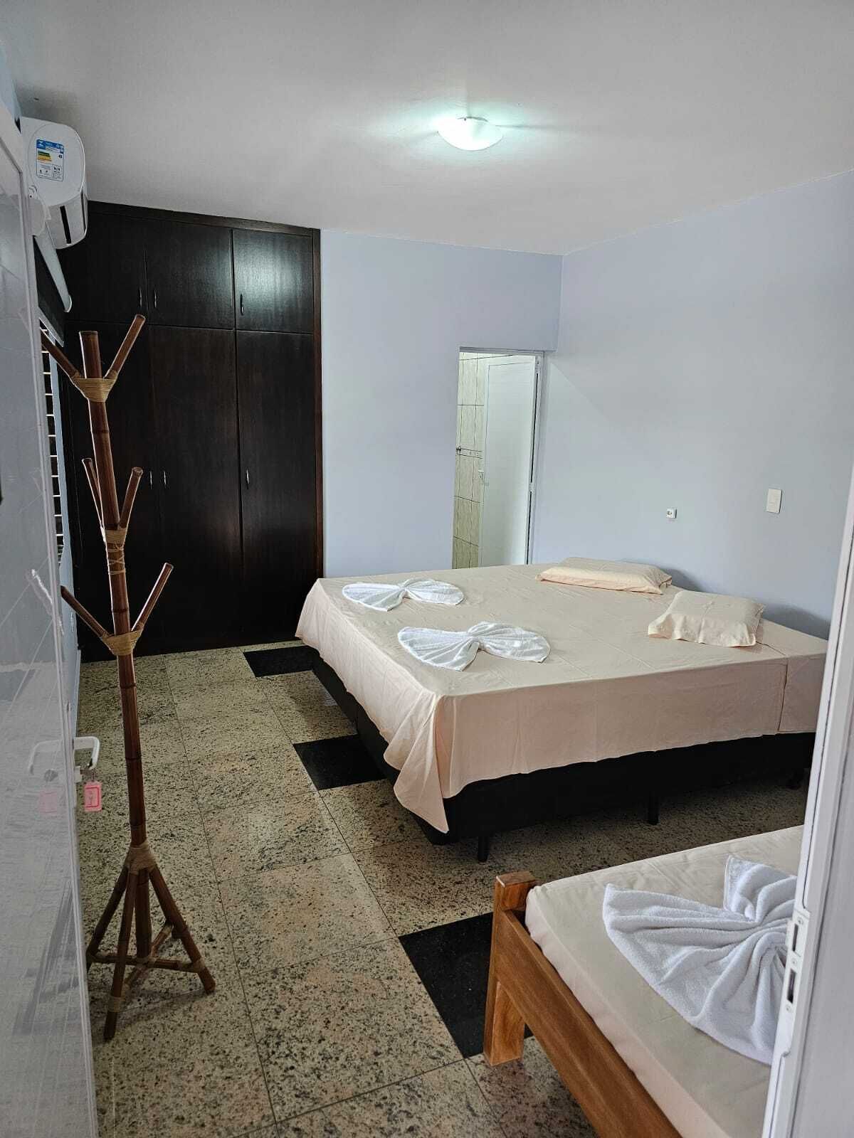 A hotel room with a bed, a wooden stool, a wardrobe, and a mirror.