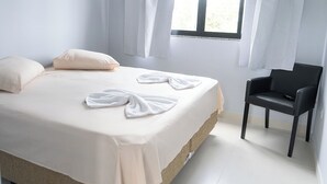 Cama bem arrumada com toalhas dispostas em forma de laço, uma cadeira preta e uma janela com cortinas.